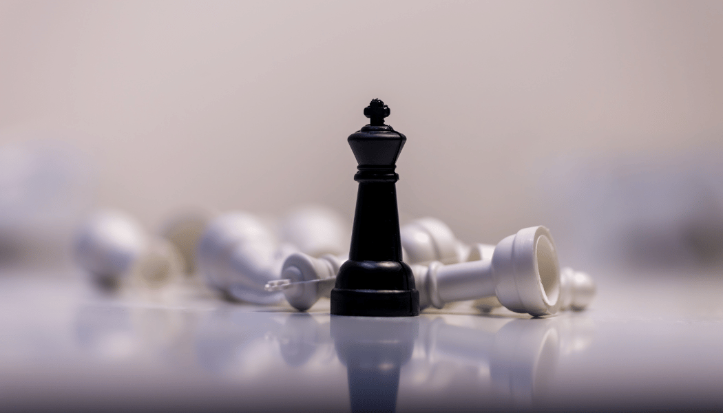 A black king piece standing amidst fallen white chess pieces